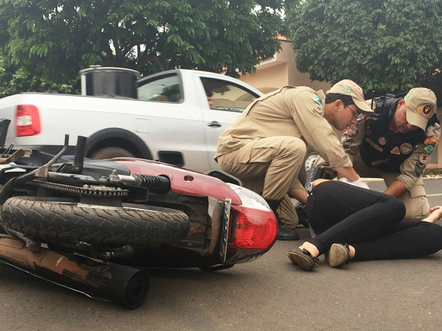 Bombeiros socorrem a jovem, caída ao solo, ao lado da motocicleta que ela conduzia (Foto: Marco Campos)