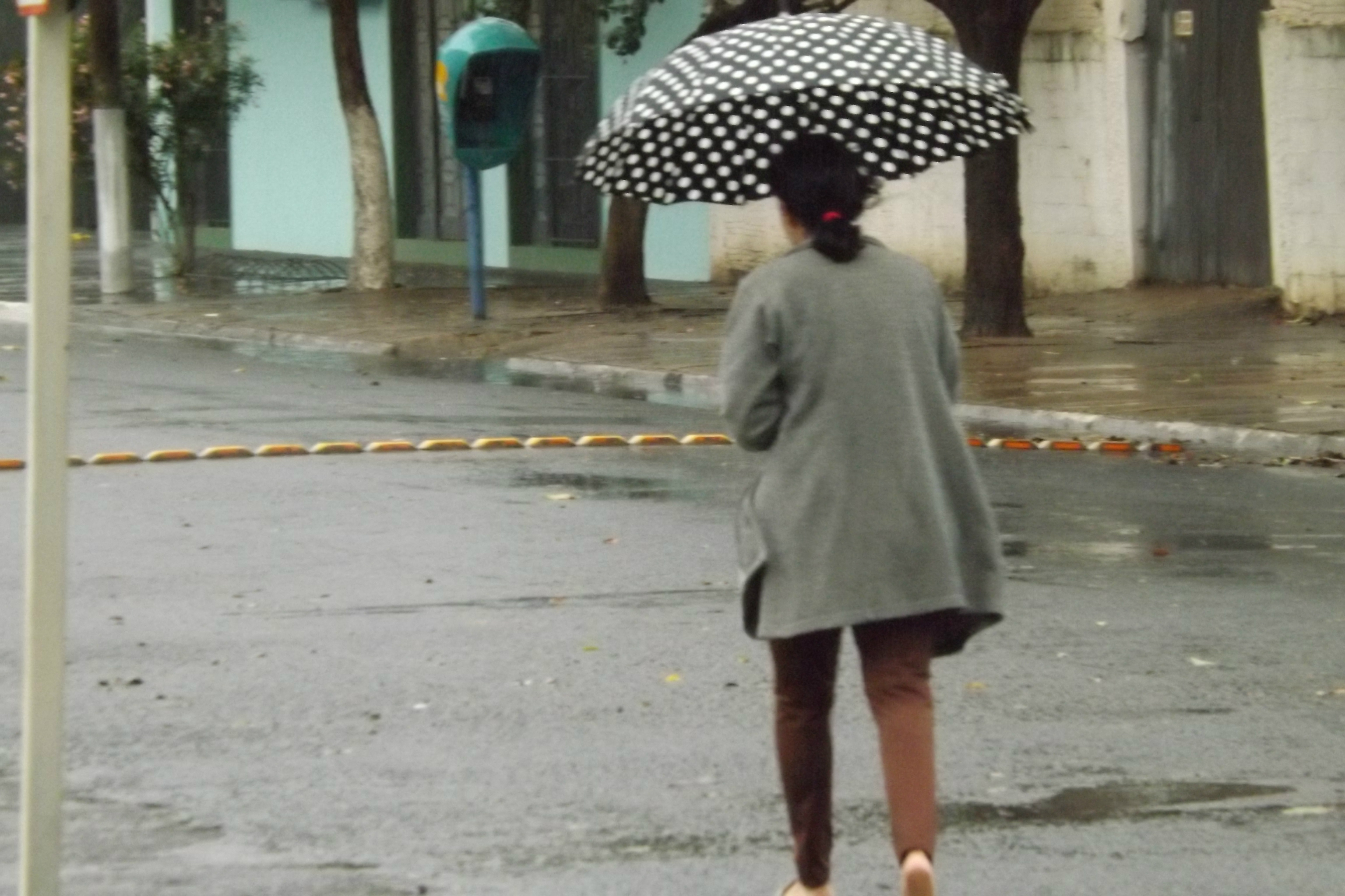 Com uma sombrinha, a mulher se protege da chuva fraca que cai sobre Três Lagoas neste momento (Foto: Edivelton Kologi)