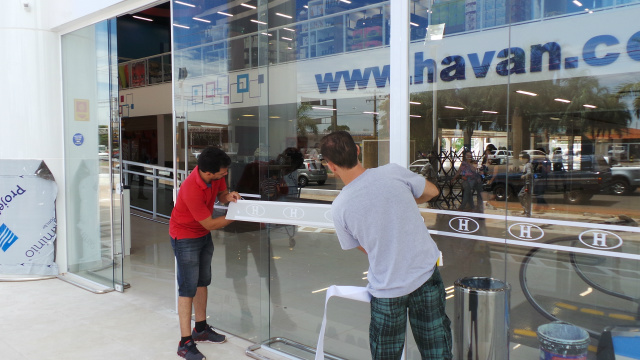 Trabalhadores acertam os últimos preparativos da decoração da loja aplicando a logomarca da empresa na vidraça de acesso ao local (Foto: Ricardo Ojeda) 