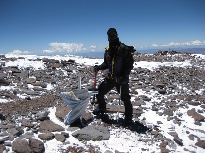 O aventureiro no cume da montanha mais alta do Hemisfério Sul, ao lado a cruz em homenagem à Força Aérea Argentina (Foto: Divulgação)