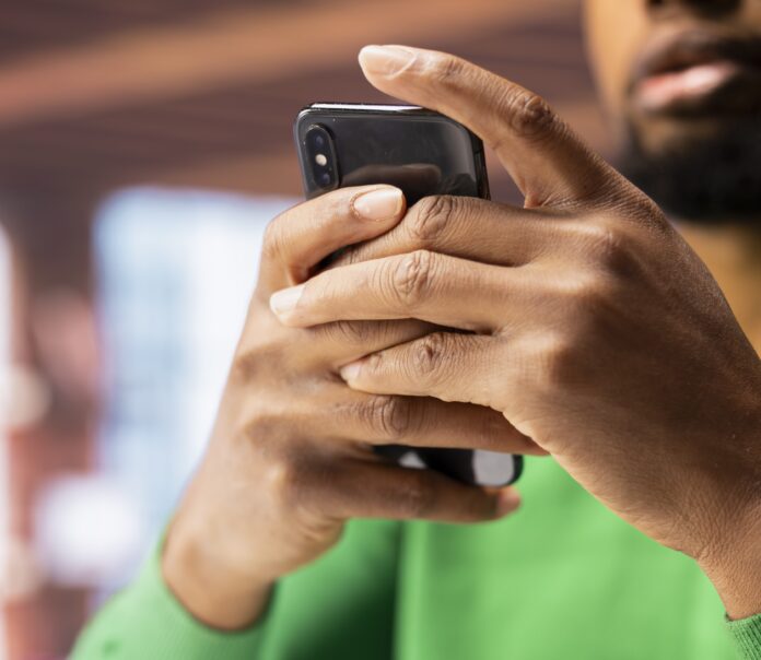 Man in home office using smartphone to compose social media posts