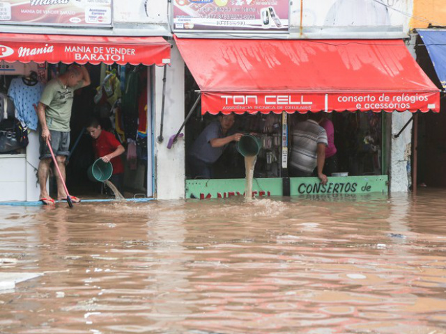 Populares tentam impedir a invasão da água depois da forte chuva que provocou diversos pontos de alagamento na Rua Padre Viegas de Menezes, no centro de Itaquera, na zona leste da capital paulista, na tarde desta quarta-feira (10). (Foto: WILLIAM VOLCOV/BRAZIL PHOTO PRESS/ESTADÃO CONTEÚDO)