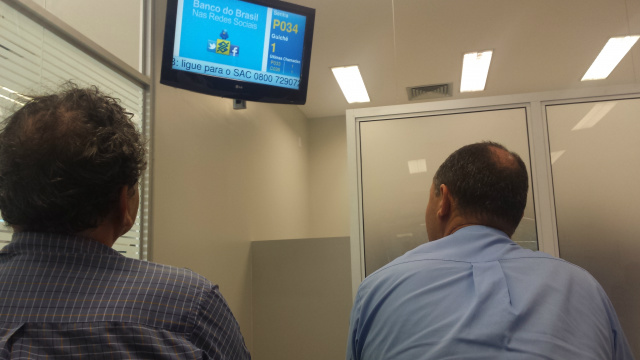 Em Três Lagoas, clientes do Banco do Brasil aguardam horas na fila para serem atendidos Clientes do Banco do Brasil olham com atenção painel da agência bancária que informa a senha de atendimento (Foto: Ricardo Ojeda)