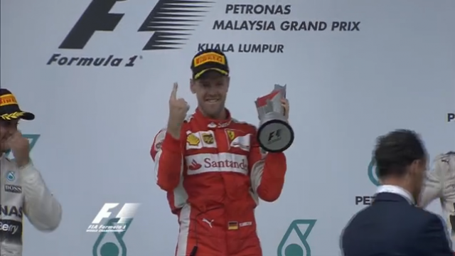 Sob olhar decepcionado de Hamilton (esquerda), Vettel aponta com o indicador sua posição na chegada, com a taça na mão (Foto: Reprodução/Rede Globo))