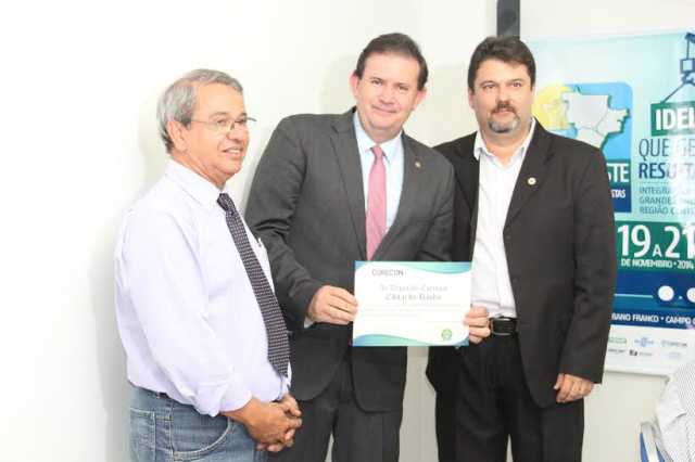 Deputado Eduardo Rocha é homenageado pelo CORECON/MS Ladeado por Thales de Souza e Jorge Tadeu, presidente e vice do Corecon/MS, Eduardo Rocha empunha a homenagem que recebeu (Foto: Divulgação)
