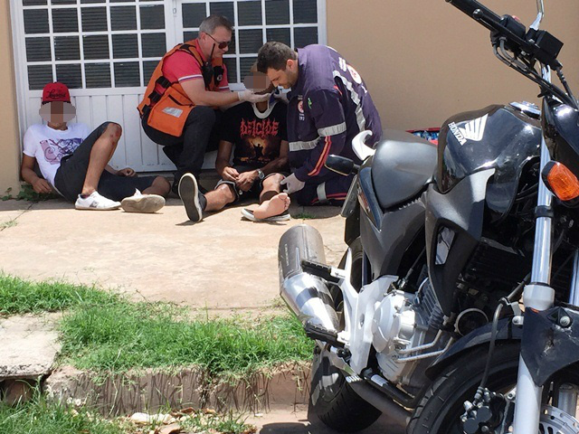 Dupla em moto sofre ferimentos em colisão contra Fiat Uno Os socorristas atendem, primeiro a vítima com suspeita de fraturas, enquanto o outro jovem aguarda ao lado; em primeiro plano, a moto envolvida no acidente (Foto: Marco Campos)