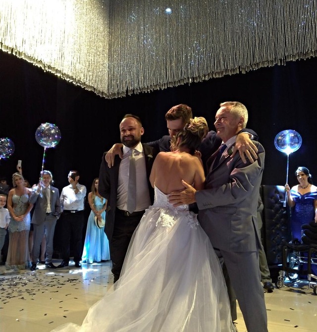 Noivo se levanta de cadeira de rodas com ajuda do pai e padrinho e dança com noiva, Veja vídeo Noivos dançando a valsa com a ajuda do pai de Hugo e de um padrinho — Foto: Cia Sinfônica/ Divulgação