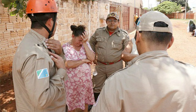 Dona Maria chora a perda dos três cachorros, sendo consolada pelos bombeiros (Foto: Midiamax News)