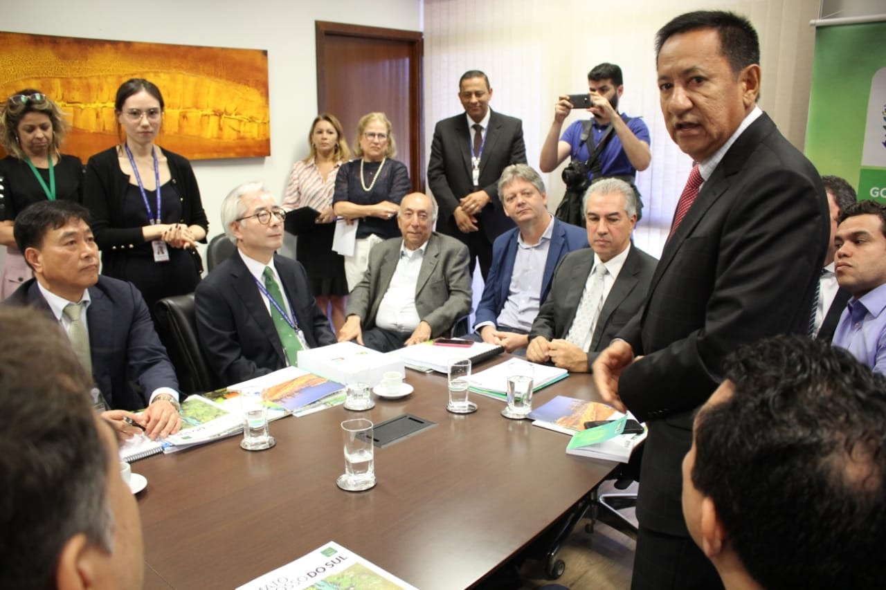 Coreanos e autoridades de Anaurilândia se reúnem com governador e confirmam investimentos de mais de R$ 6 bilhões Prefeito de Anaurilândia, Edinho Takazono (em pé, à direita) esteve com o Governador Reinaldo Azambuja (sentado à cabeceira da mesa), o secretário Jaime Verruck (ao lado direito do governador) e os empresários sul-coreanos, também sentados à mesa. Fotos: Chico Ribeiro